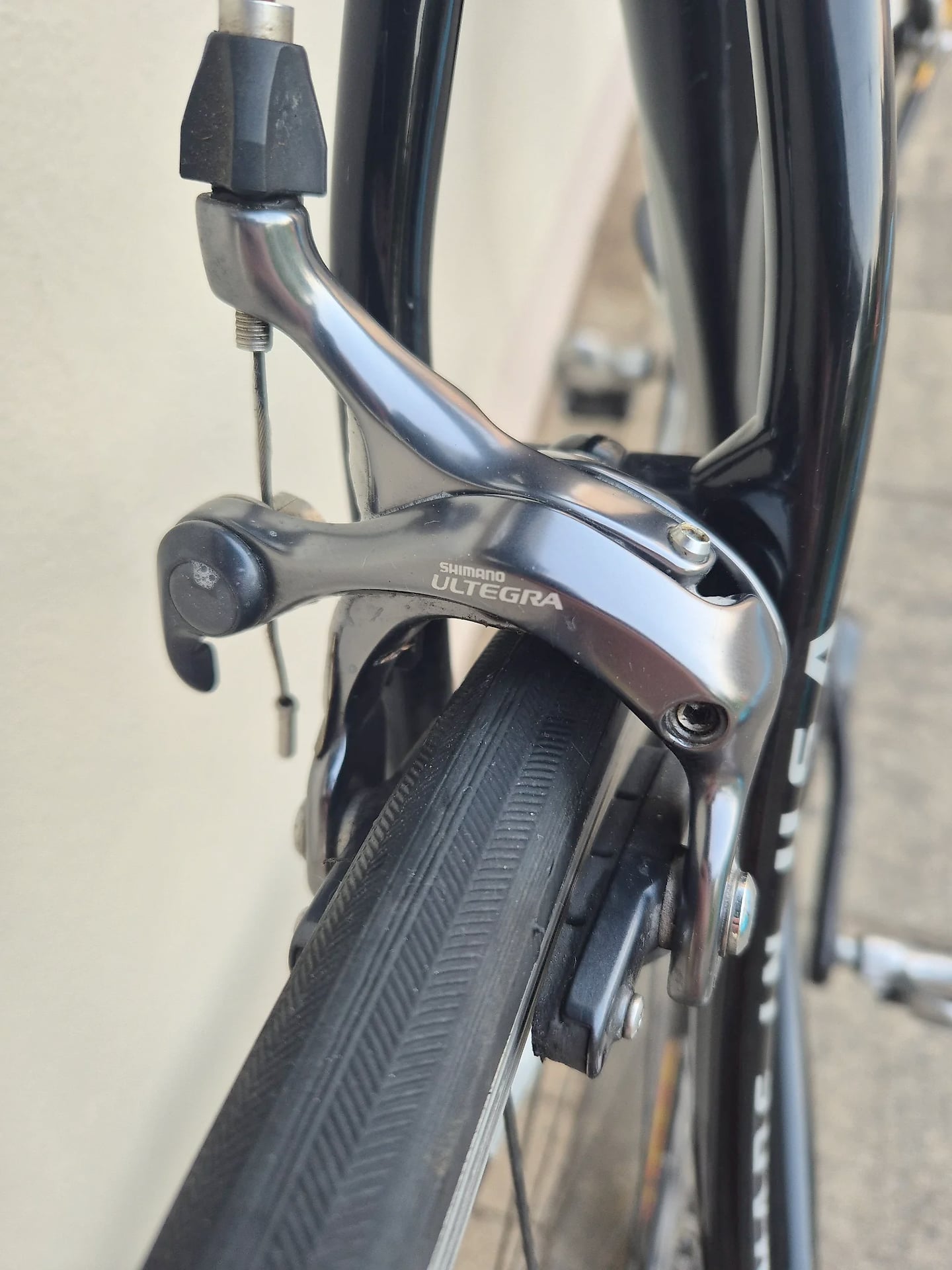 Shimano Ultegra brake caliper on black road bike, close-up of front brake assembly and tyre, drive side angle against neutral background.