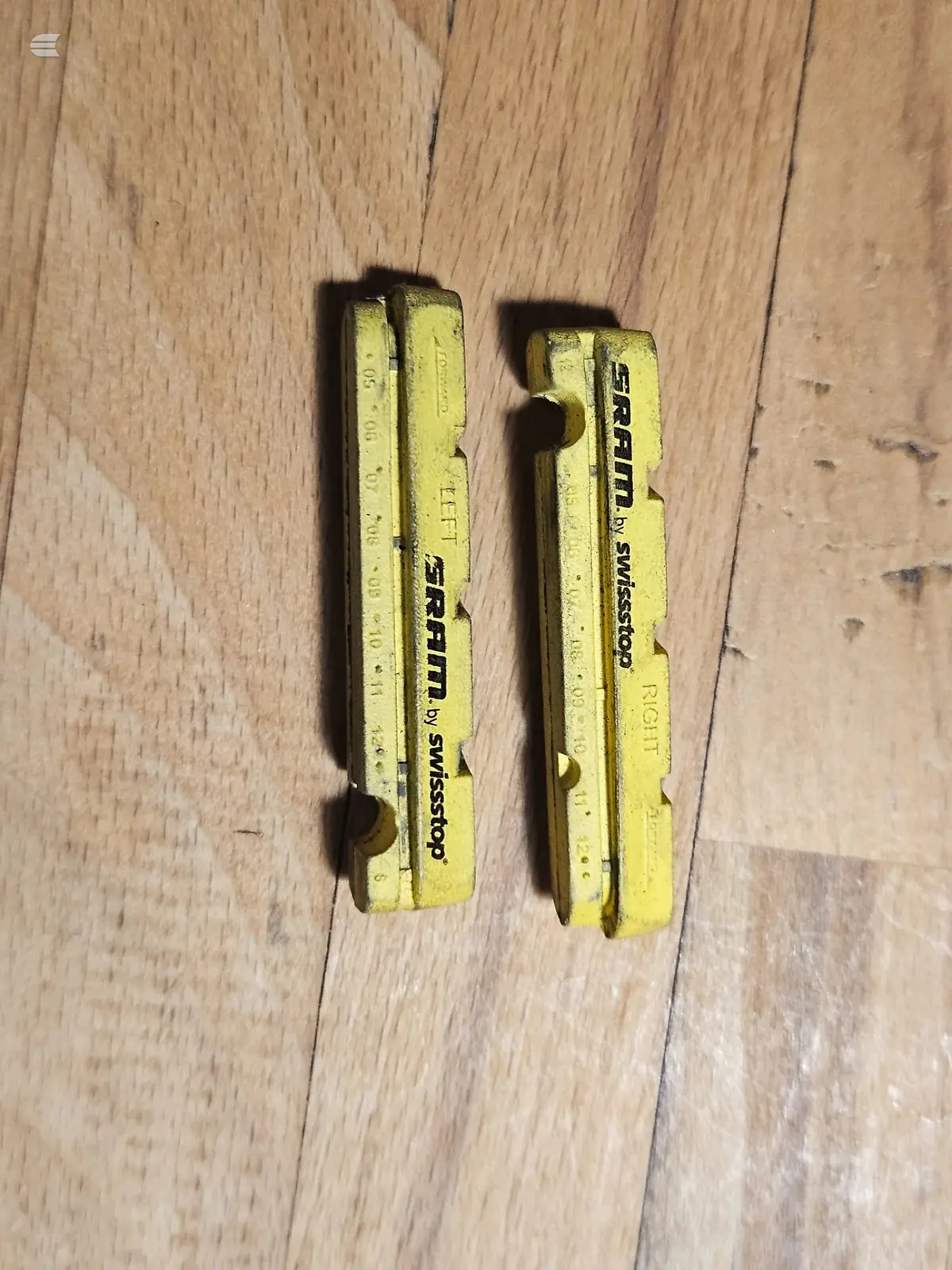 Two yellow Sram brake calipers on wooden floor, close-up detail shot.