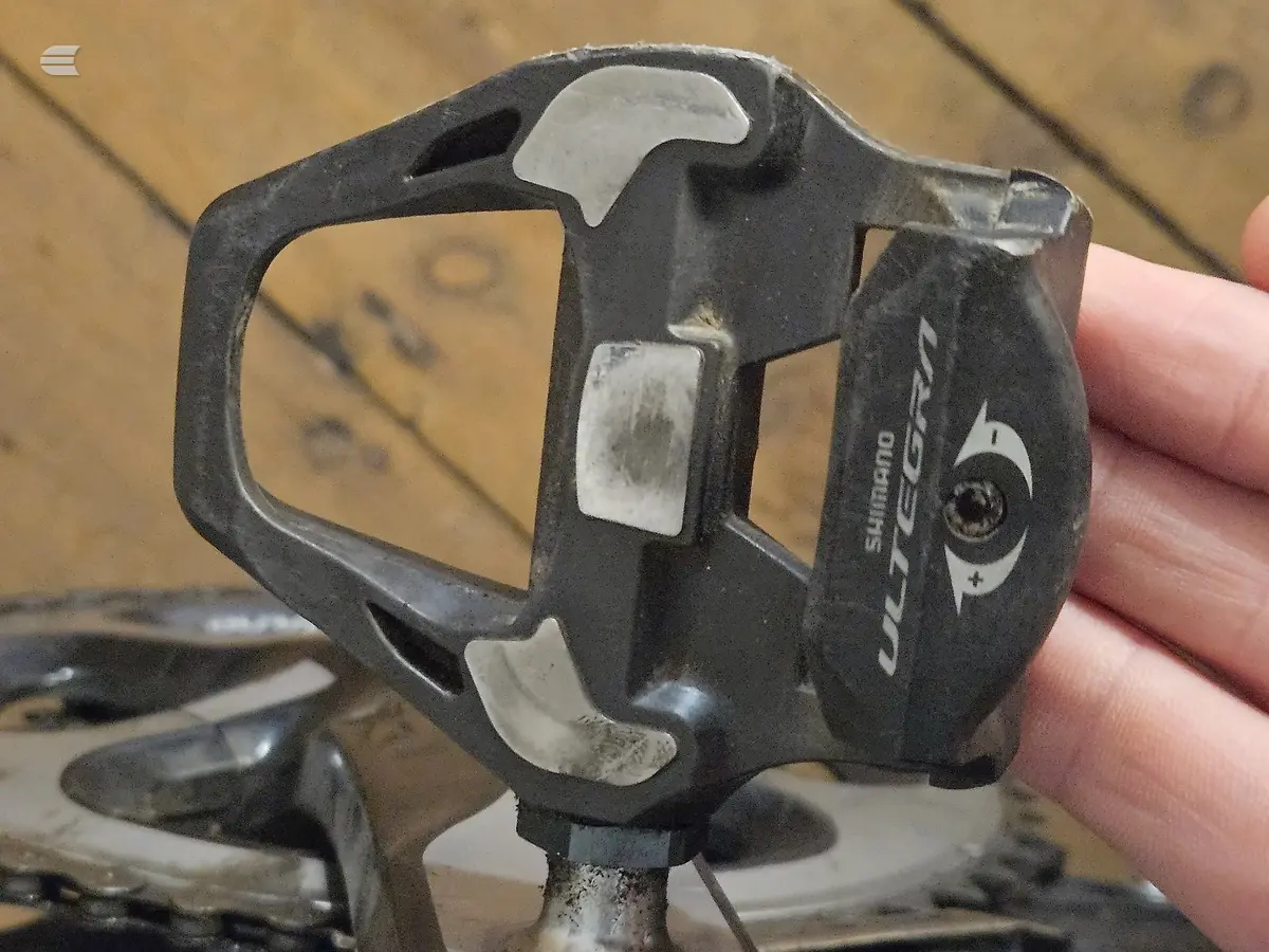 Shimano Ultegra PD-6700 SPD-SL pedal with cleats, close-up on wooden workbench, drive side.