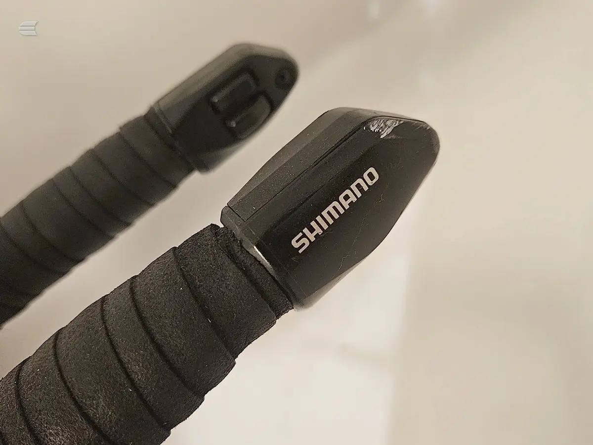 Close-up of Shimano brake lever and wrapped handlebar grip on black drop bars, angled view against neutral background.