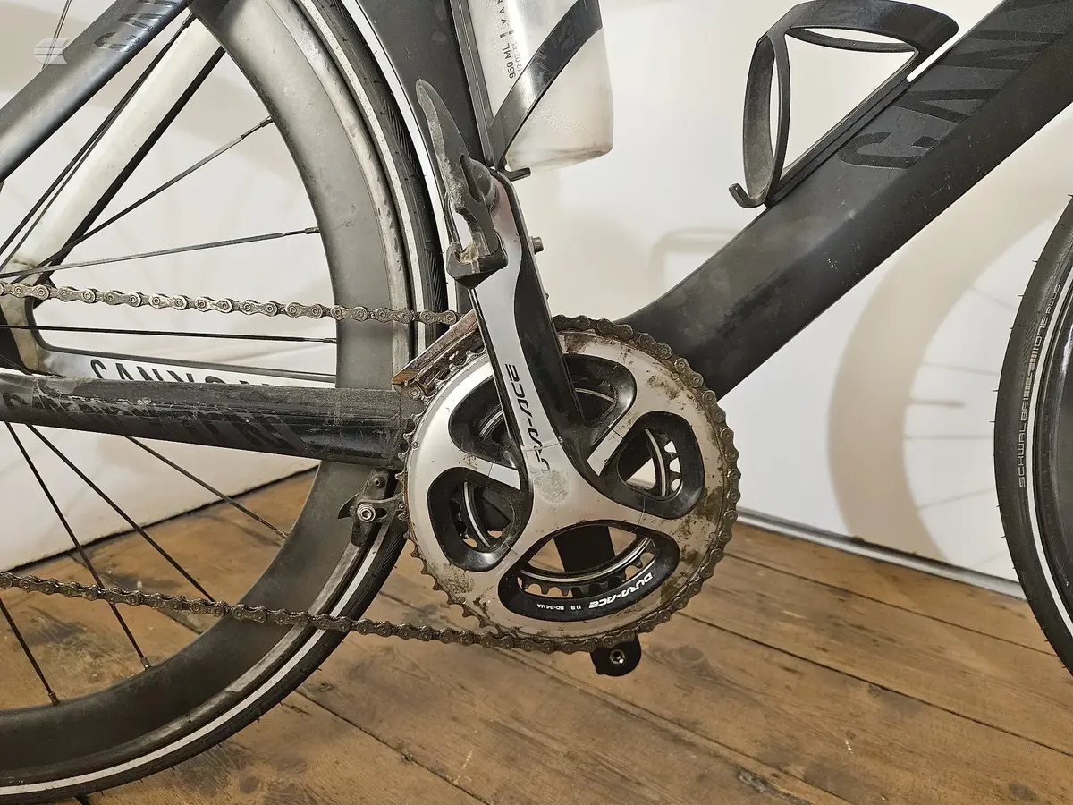 Shimano Ultegra crankset and chainrings on a black road bike, drive side close-up, wooden floor background.