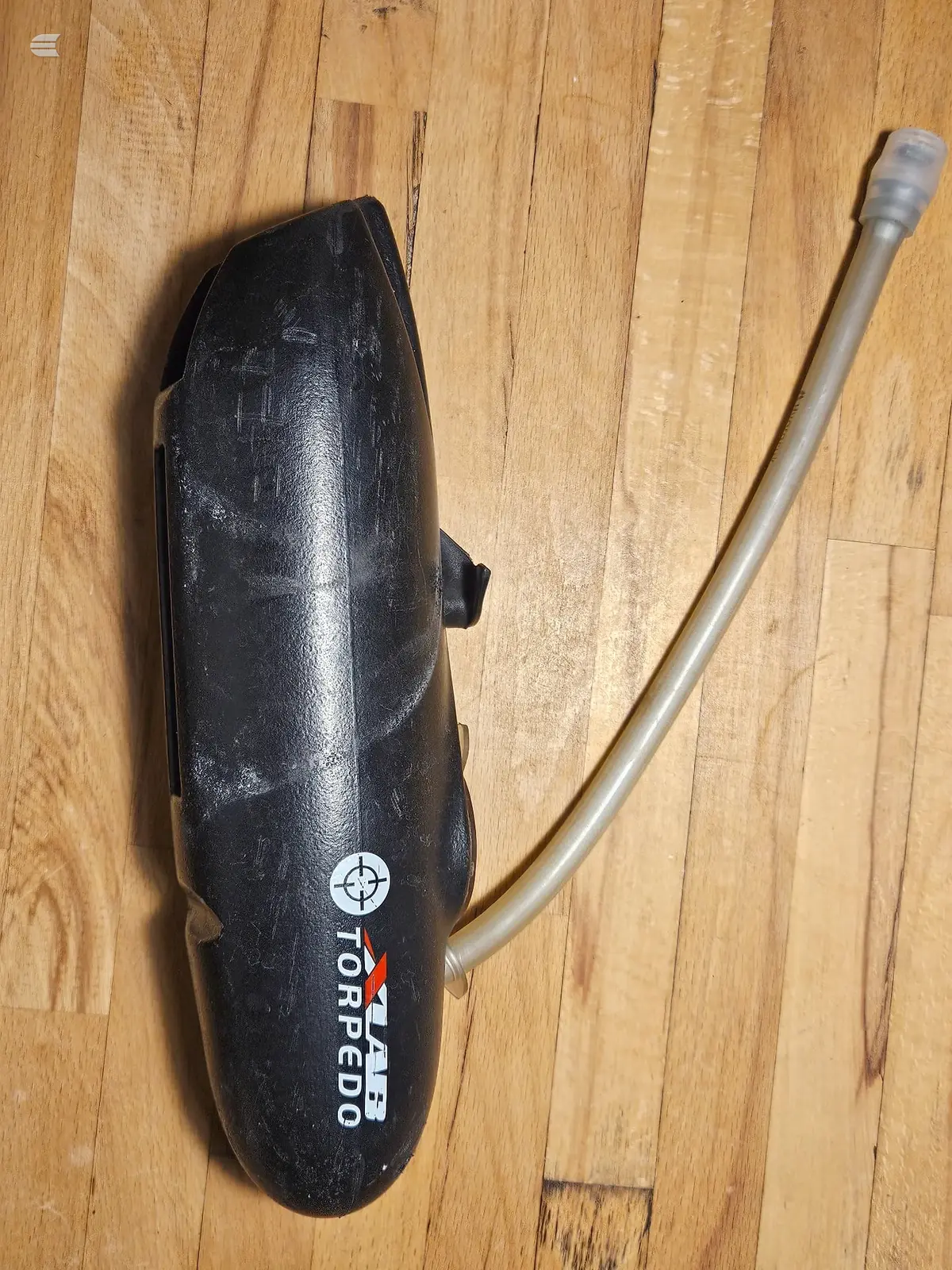 Black torpedo-shaped bicycle horn with curved metal tube attachment, on wooden floor.