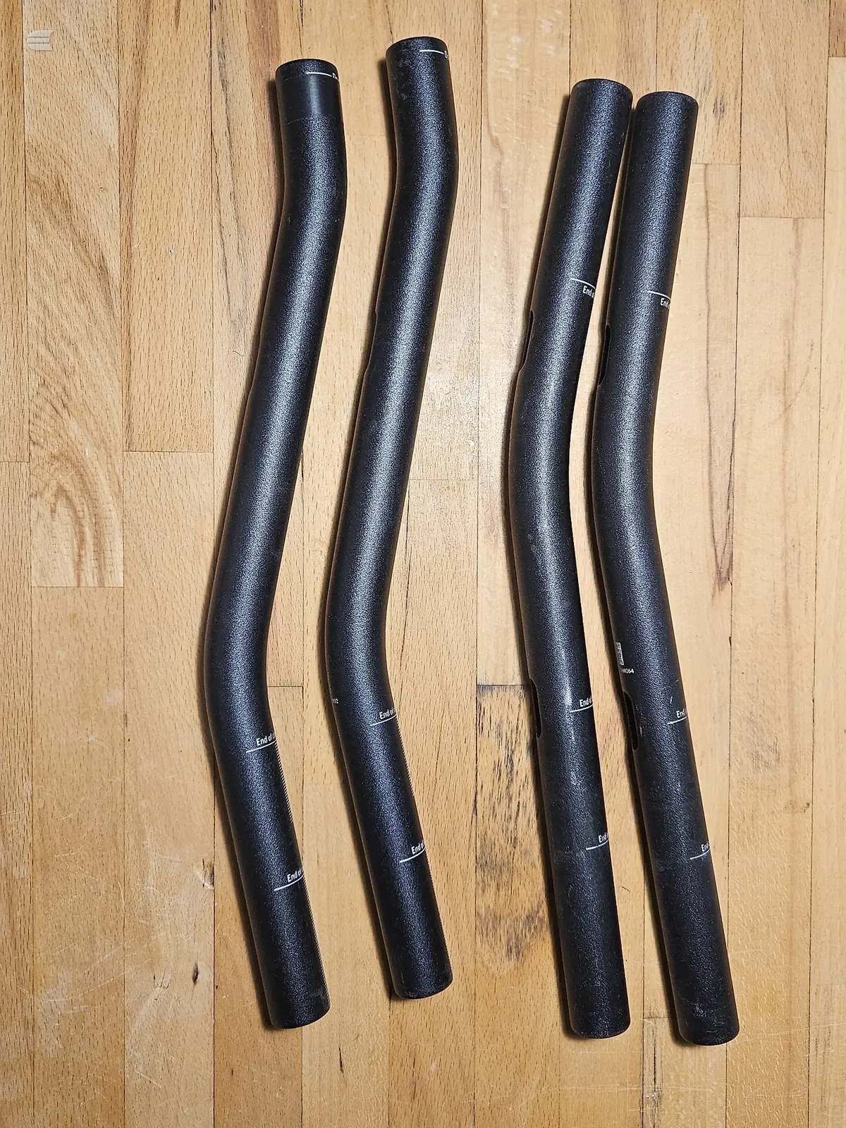 Four black bicycle seat posts with grip tape, arranged in pairs on a wooden floor.