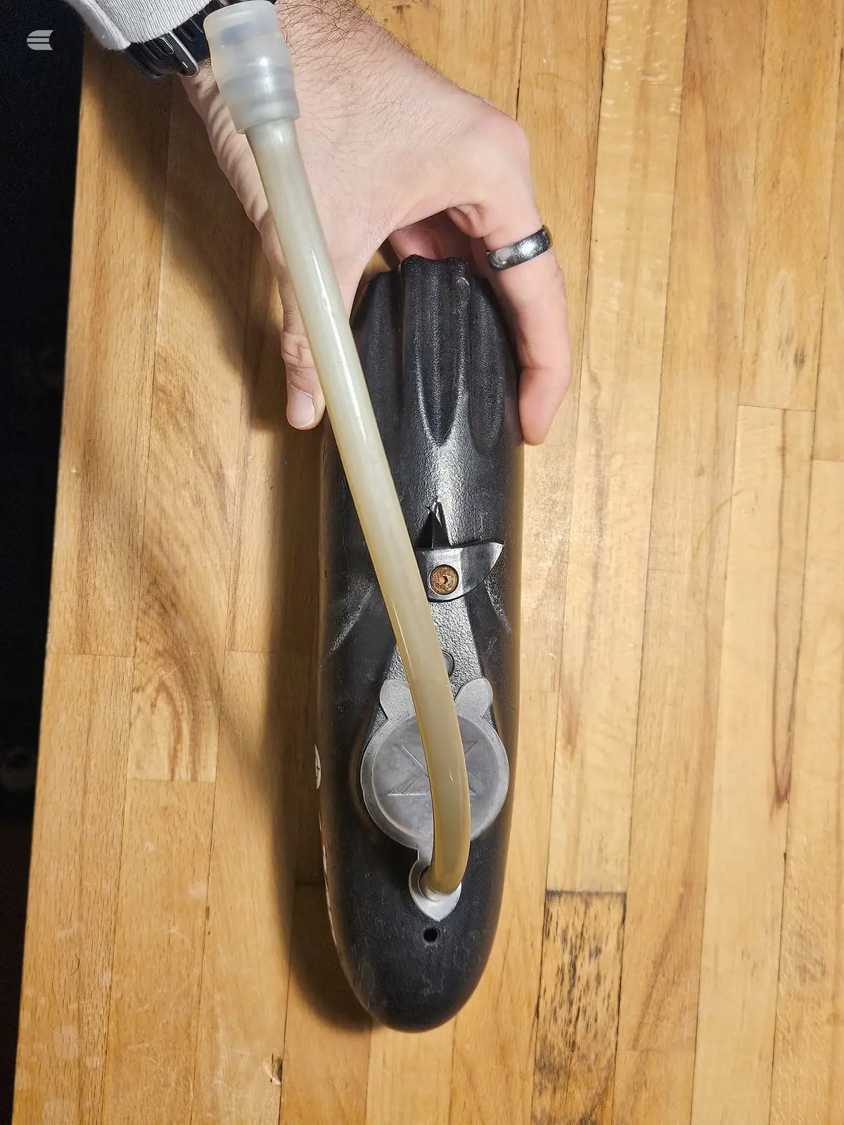 Black leather saddle with metal hardware and tan canvas tool bag attached, mounted on bicycle frame, wooden floor background.