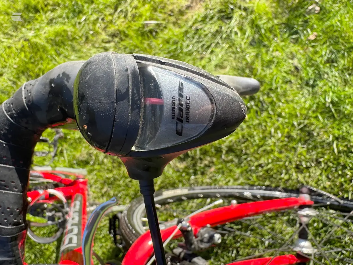 Shimano Deore drive shifter mounted on red and black drop bar bicycle, close-up against green grass background.