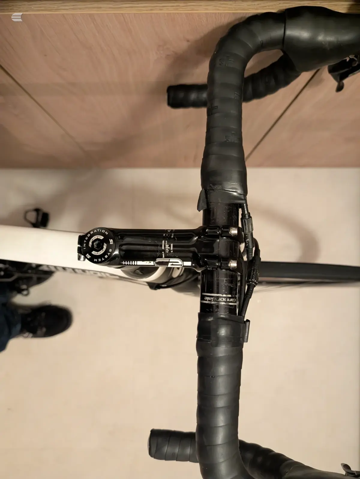 Black drop-bar road bike handlebars and brake lever assembly, close-up detail shot against white wall background.