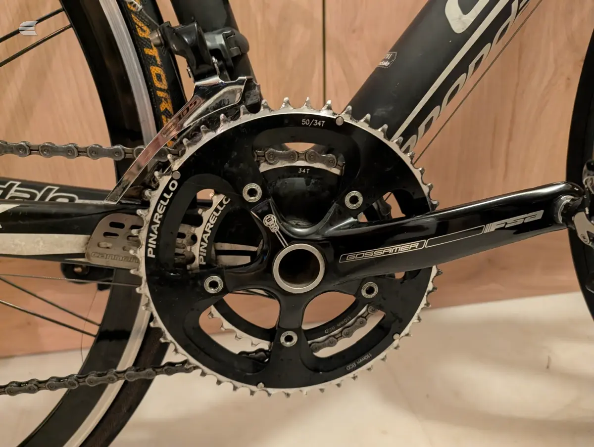 Close-up of Gossamer crankset and chainrings on a black road bike, drive side, wooden floor background.