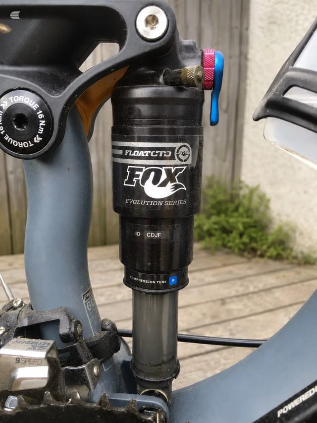 Fox Evolution Series rear shock with float CTD damper on blue full-suspension mountain bike, detail view showing compression tune adjuster and blue/red remote