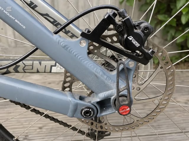 Close-up of disc brake caliper and rotor on grey hardtail mountain bike, drive side, outdoors on concrete.