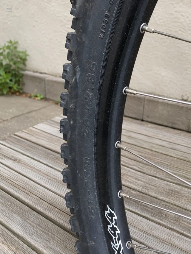 Black Avanti mountain bike tyre, close-up side view on wooden decking, showing tread pattern and sidewall branding with spoke nipples visible.