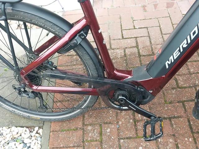 Maroon and grey step-through e-bike on brick paving, drive side, parked outdoors.
