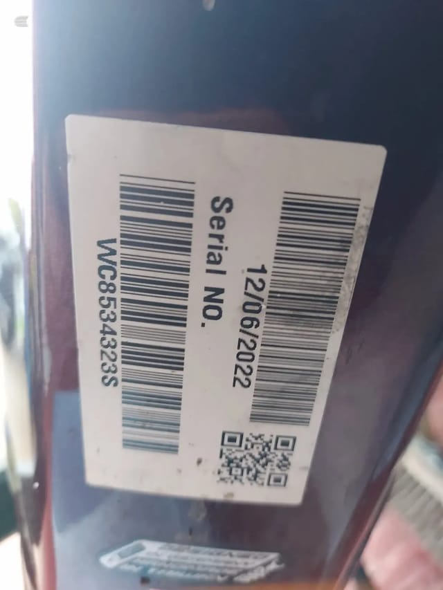 Shipping or delivery label with barcode, serial number, and QR code on a dark surface, angled view.