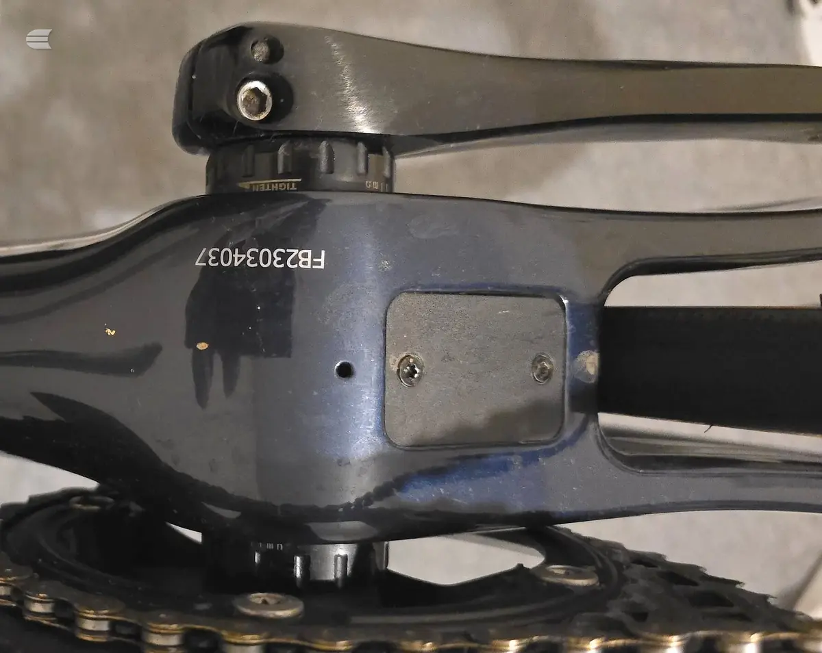 Close-up of bicycle derailleur and rear cassette on dark frame, drive side, against concrete background.