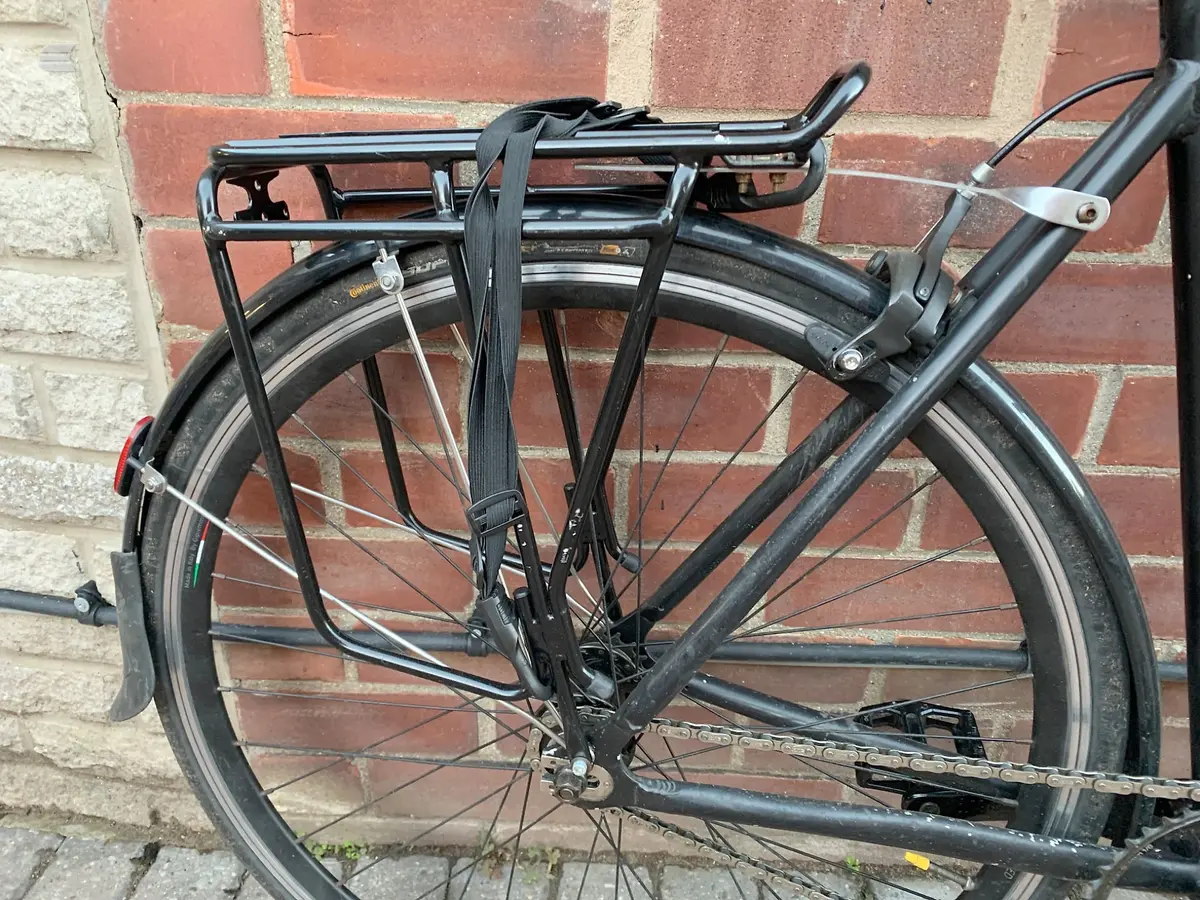 Black hybrid bike with rear rack and mudguards, mounted on brick wall, non-drive side view.