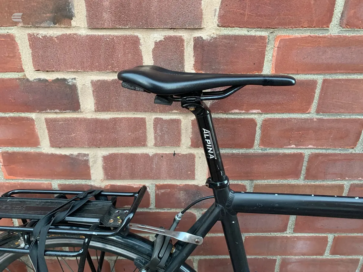 Black Selle Italia saddle and seatpost on a black-framed bike, mounted against a red brick wall with white mortar joints.
