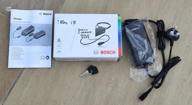 Bosch bicycle charger box, instruction manual, power cable, and keys laid out on carpet.
