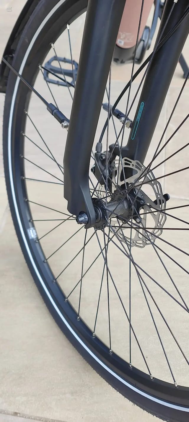 Close-up of front wheel and lower frame of black gravel or hybrid bike, drive side, on concrete ground.