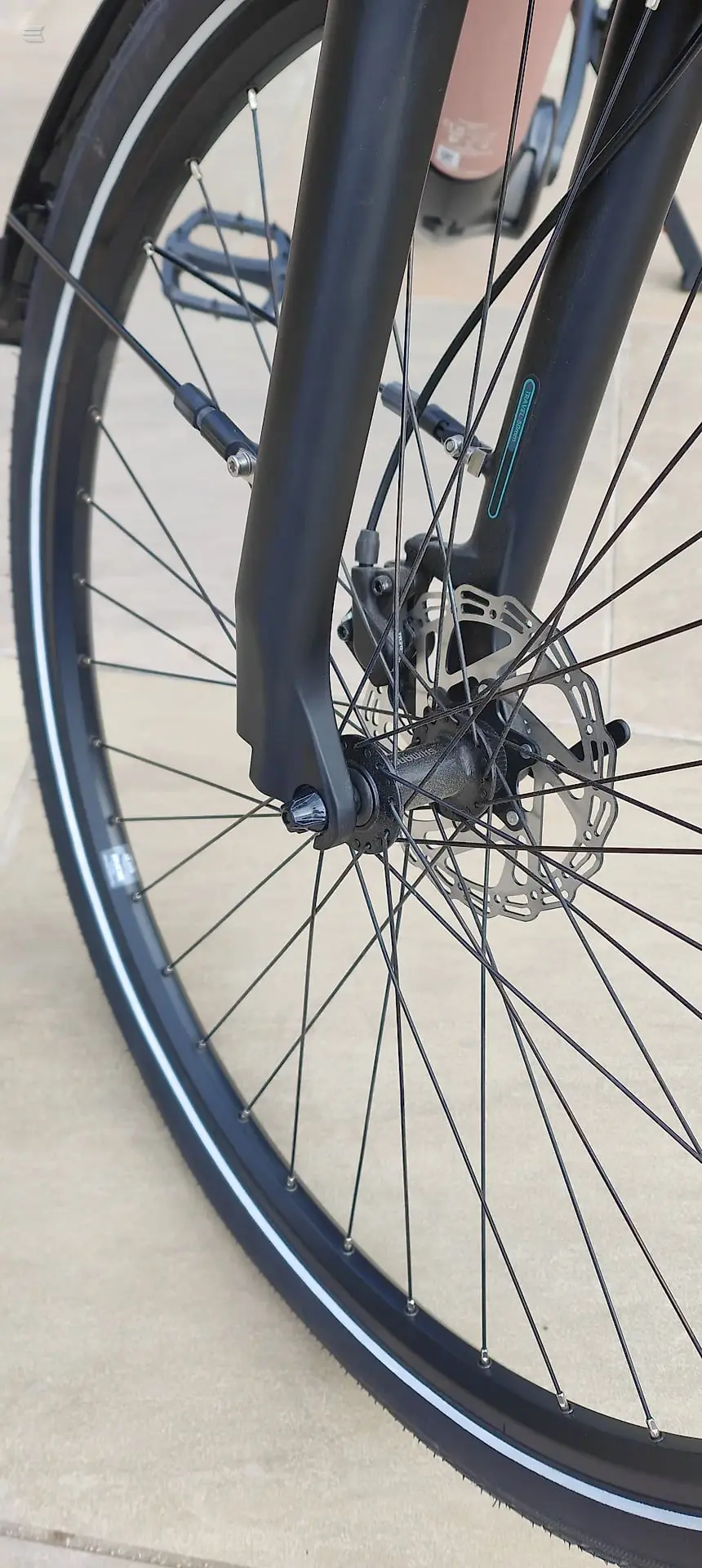 Close-up of front wheel and lower frame of black gravel or hybrid bike, drive side, on concrete ground.