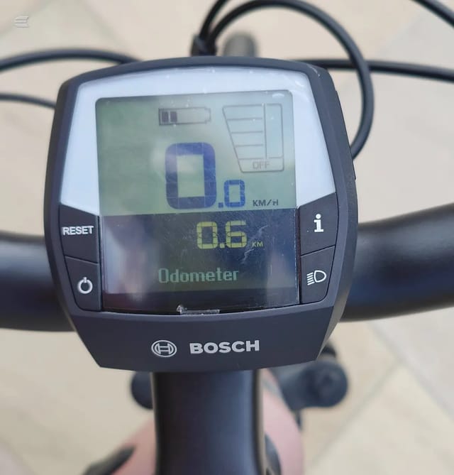 Bosch electric bike display console mounted on handlebars, showing odometer reading 0.6 km and speed 0.0 km/h, against a beige background.
