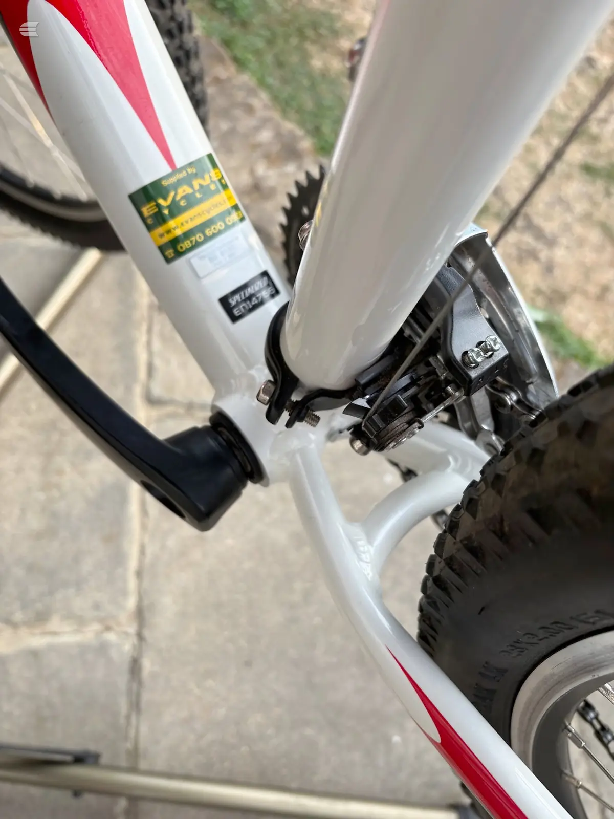 White and red hybrid bike, close-up of front brake caliper and fork, non-drive side, on pavement with grass visible.