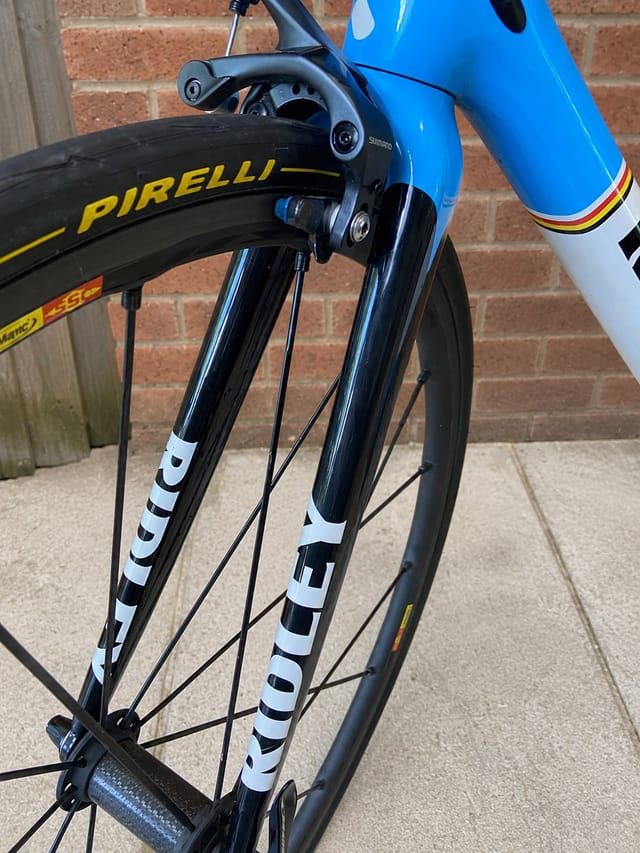 Blue and white road bike with Pirelli tyres, non-drive side view, leaning against brick wall and concrete ground.