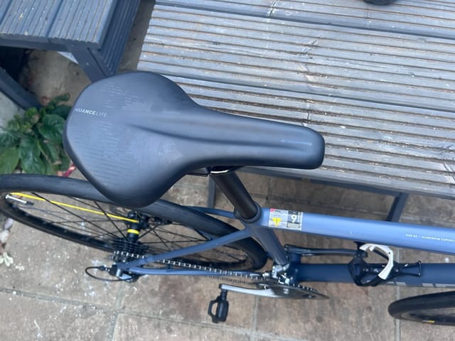 Blue Nuance Lite aluminium bike on concrete, drive side, against corrugated metal shutter. Saddle and partial frame in focus.