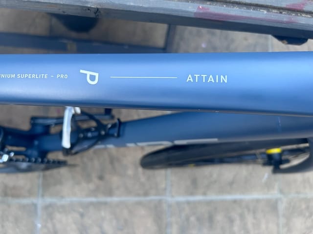 Blue aluminium Superlite Pro bicycle frame tube close-up, showing brand text and model name on the seat tube against a concrete background.