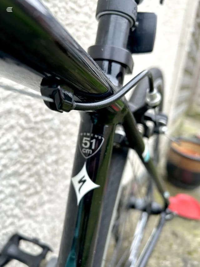Close-up of black drop handlebars and brake lever on a green-framed road bike, drive side, against a stone wall.