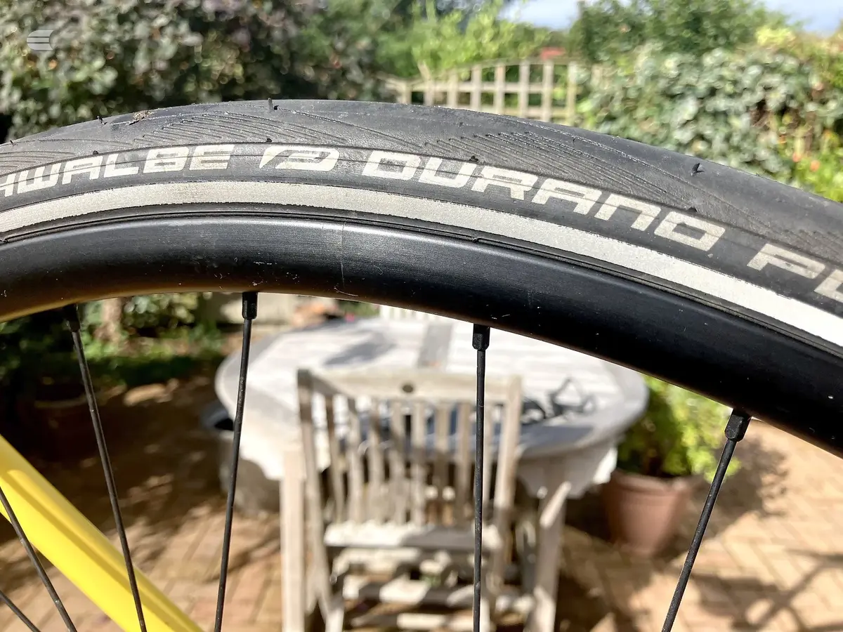 Close-up of a black Schwalbe Pro One road bike tyre on a yellow-framed bike, angled view in a garden setting with blurred background.