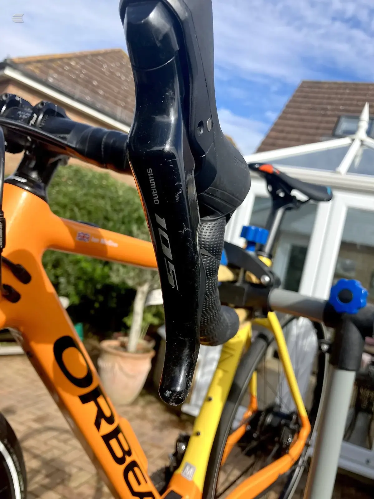 Black Shimano drop bar brake lever and grip on orange Orbea road bike frame, close-up detail shot in driveway setting.