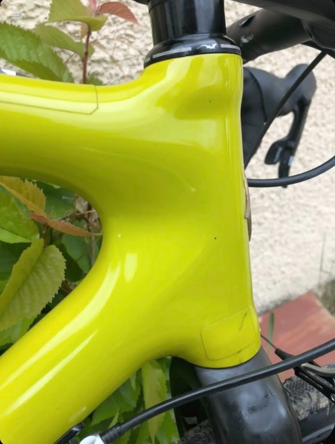 Bright yellow bicycle frame close-up, non-drive side, showing head tube and fork junction with black headset and cable routing against blurred pavement and