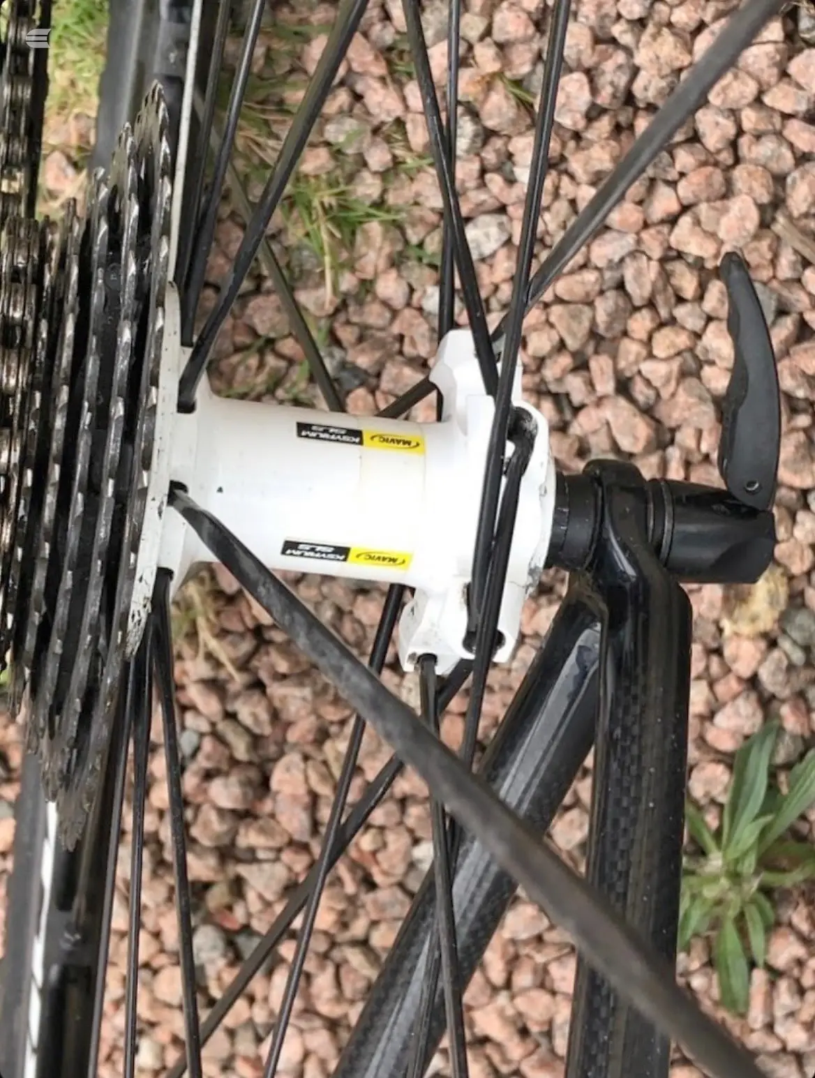 White and black disc brake caliper and rotor on bicycle frame, close-up detail shot against gravel background.