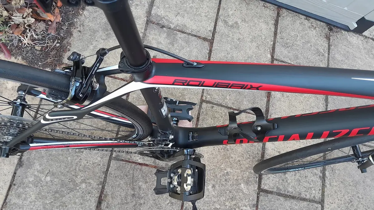 Black and red Specialized road bike on concrete paving, drive side view, handlebars and saddle visible, pedals engaged.