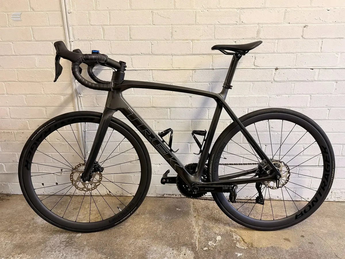 Black gravel or endurance road bike on concrete ground against a cream brick wall, drive side view.