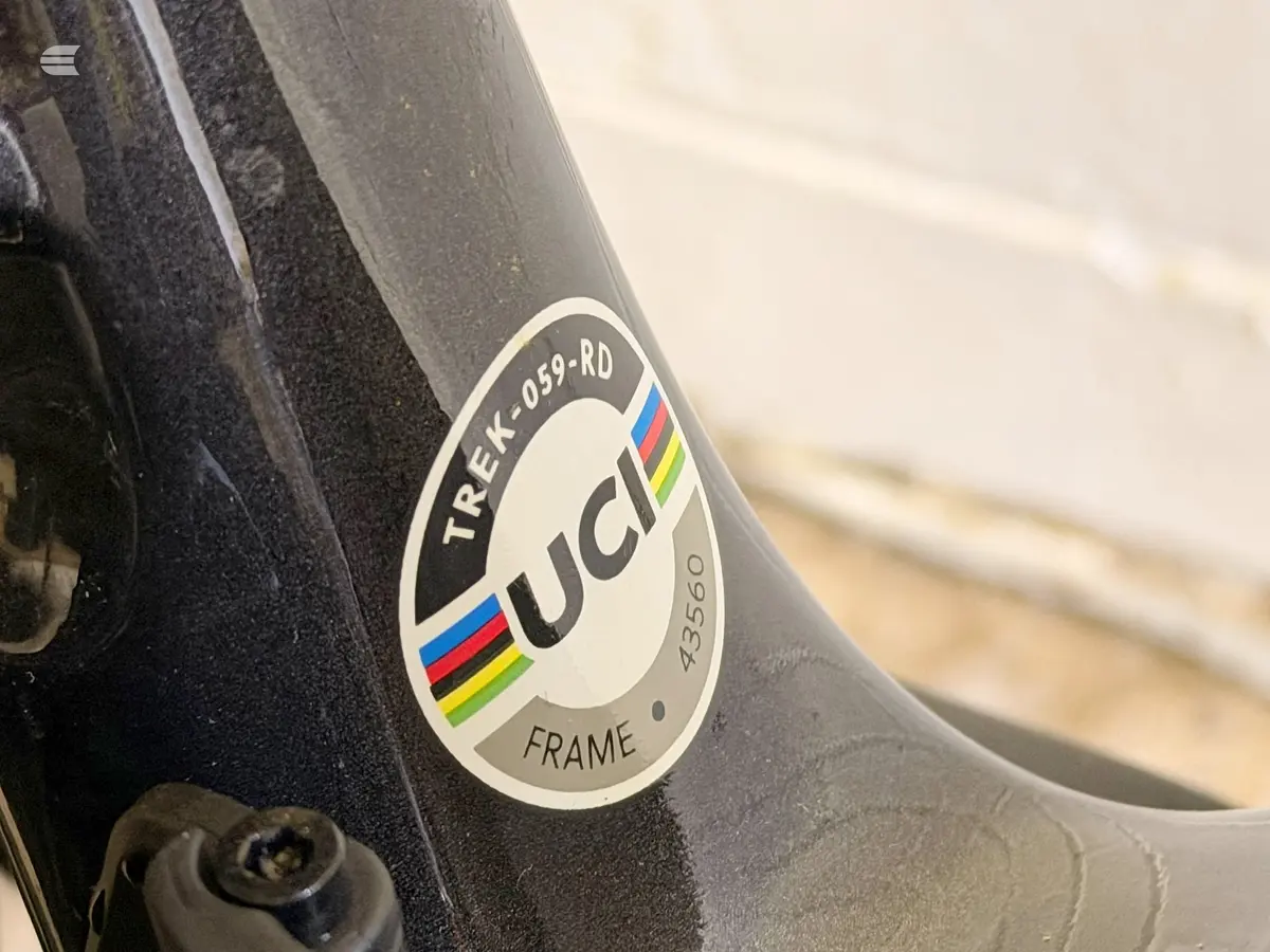 Close-up of UCI frame certification sticker on black bicycle frame, showing Trek 059-RD model number and rainbow stripes, mounted on frame tube.