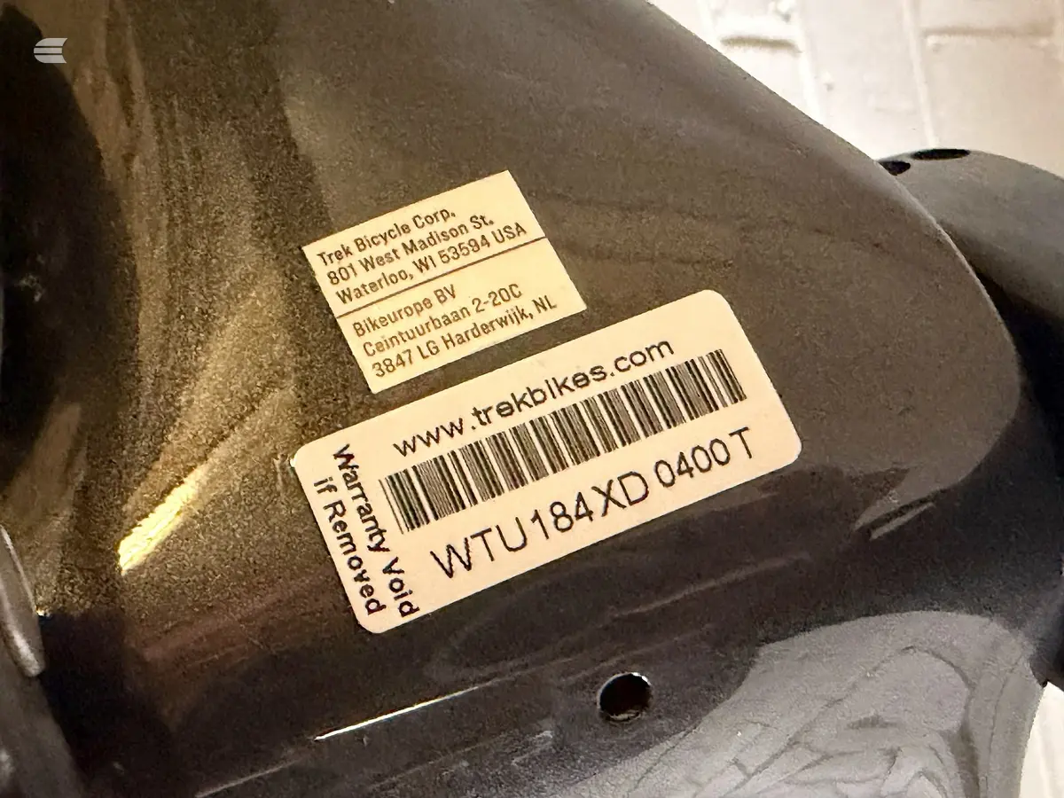 Trek Bicycle Corp. warranty and identification labels on black bike component, showing barcode and distributor contact details.