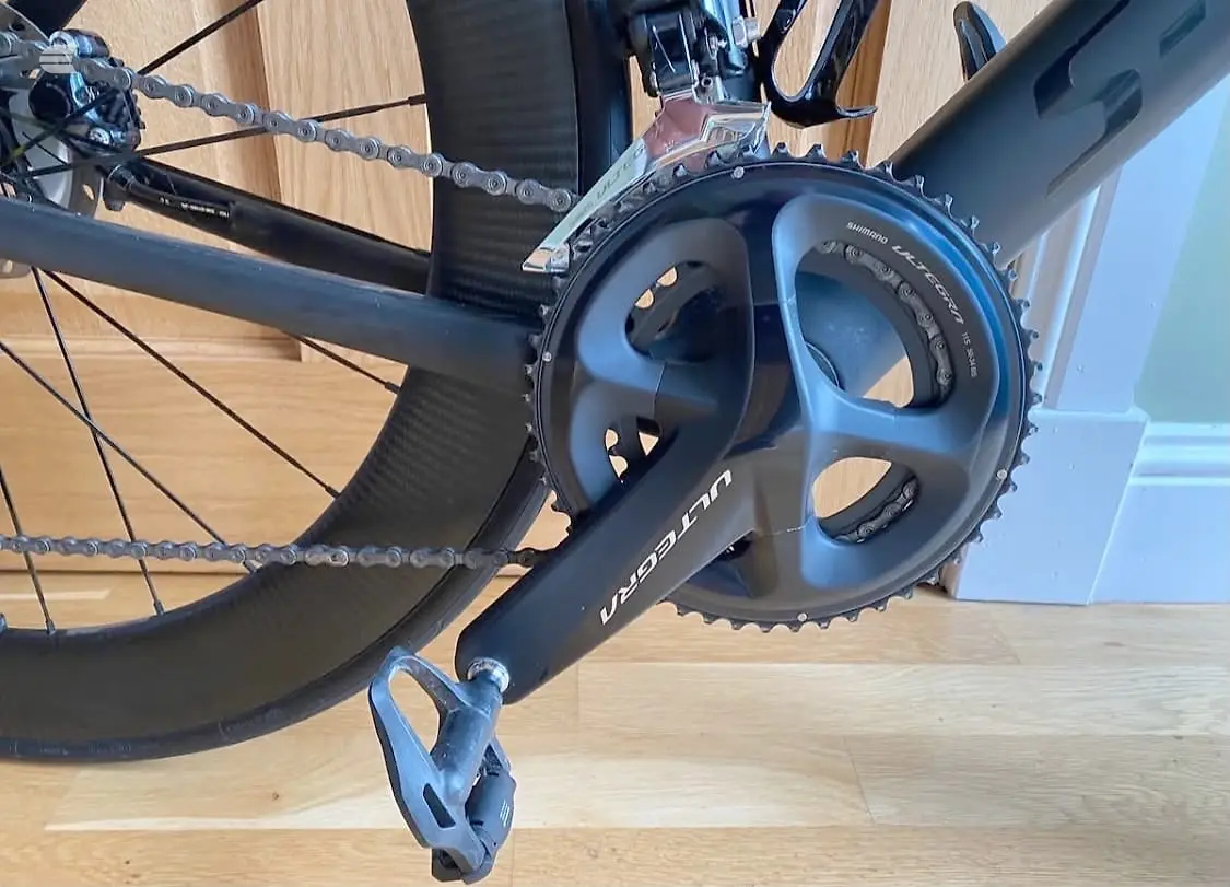 Shimano Ultegra crankset and chainrings on a black road bike, drive side, indoors on wooden floor.