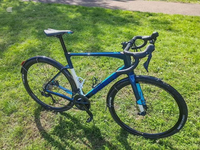 Blue and black Ribble road bike on grass, drive side view, handlebars and saddle visible.