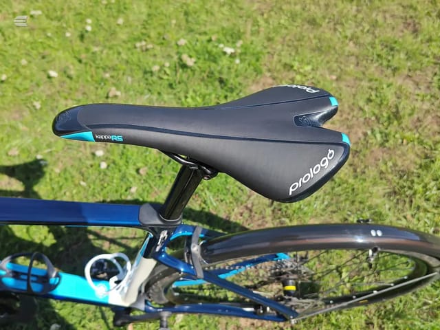 Black and cyan Prologogo Kappa RS saddle on blue and cyan road bike, non-drive side, outdoors on grass.