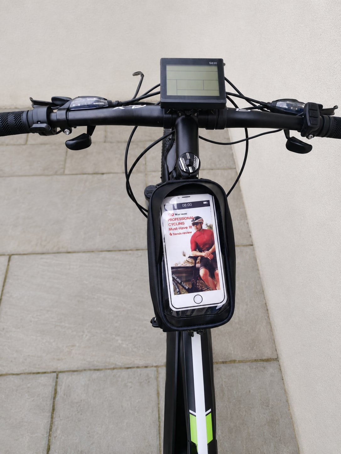 Black and lime-green electric bike with integrated smartphone mount and digital display on handlebars, viewed head-on against a light stone wall.