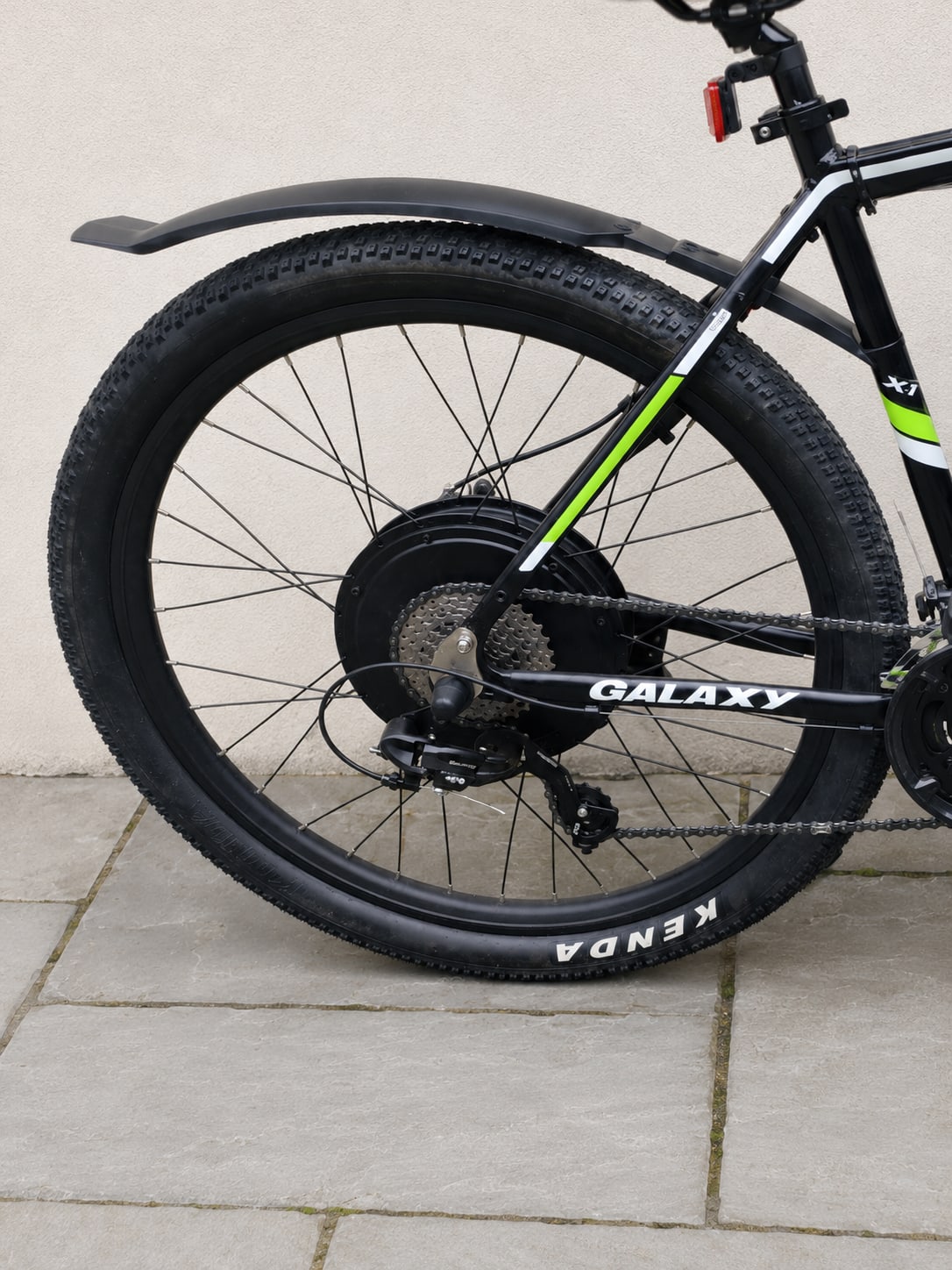 Black and neon-green Galaxy hardtail mountain bike, rear wheel close-up on paved ground, drive side, showing Kenda tyre and cassette.