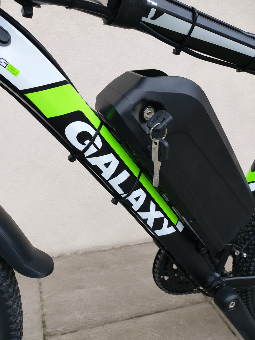 Close-up of black e-bike battery pack with key lock on neon-green and black frame, mounted on down tube, non-drive side view.