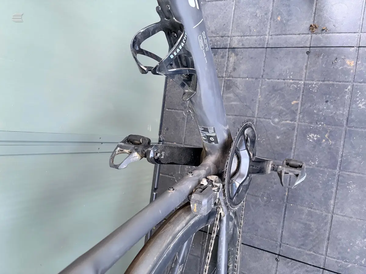 Grey gravel or cyclocross bike on tiled floor, drive side, leaning against pale wall. Rotated 90 degrees.