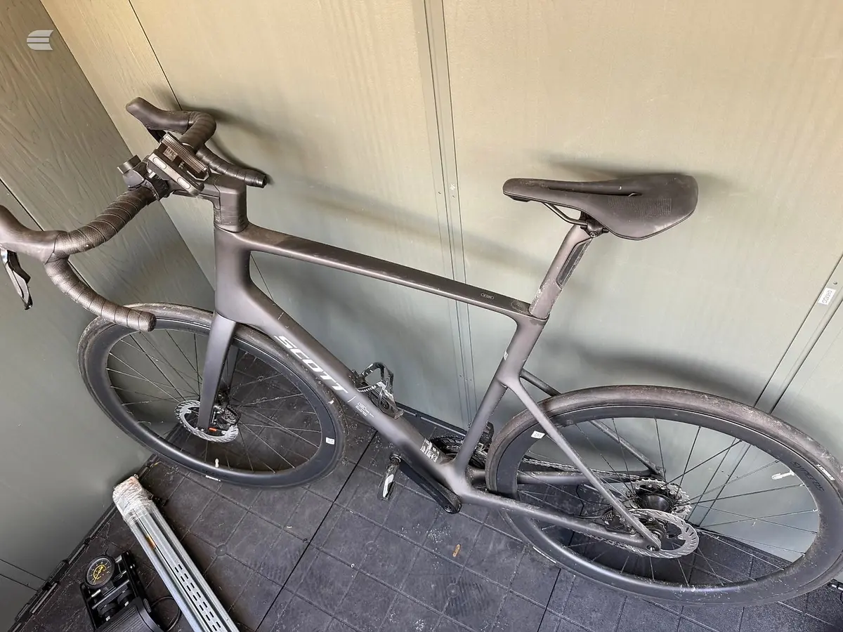 Silver gravel bike on wall mount, drive side, against beige panelled wall in garage or storage space.