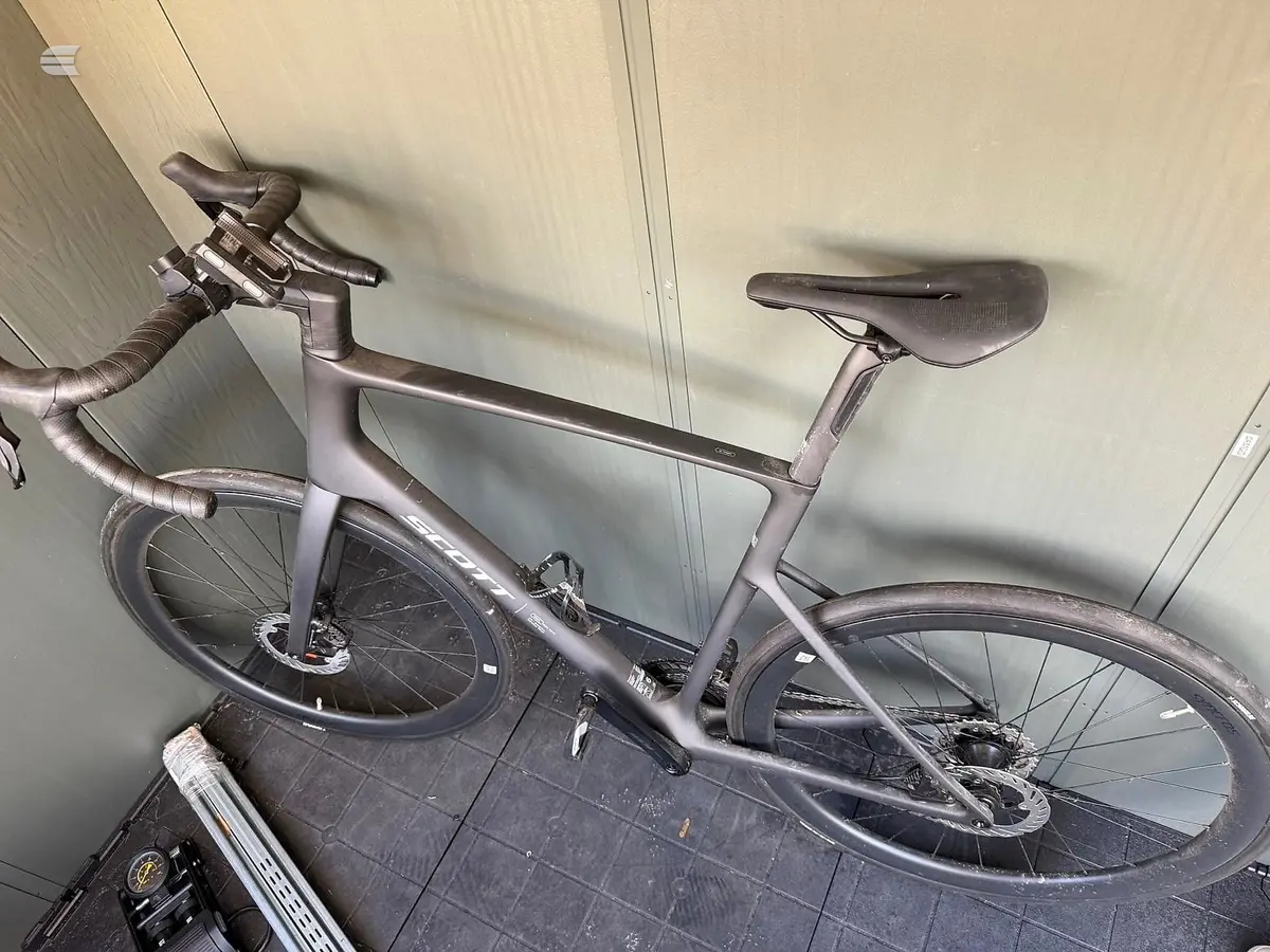 Grey gravel bike on wall mount, drive side, against white panelled wall in garage setting.