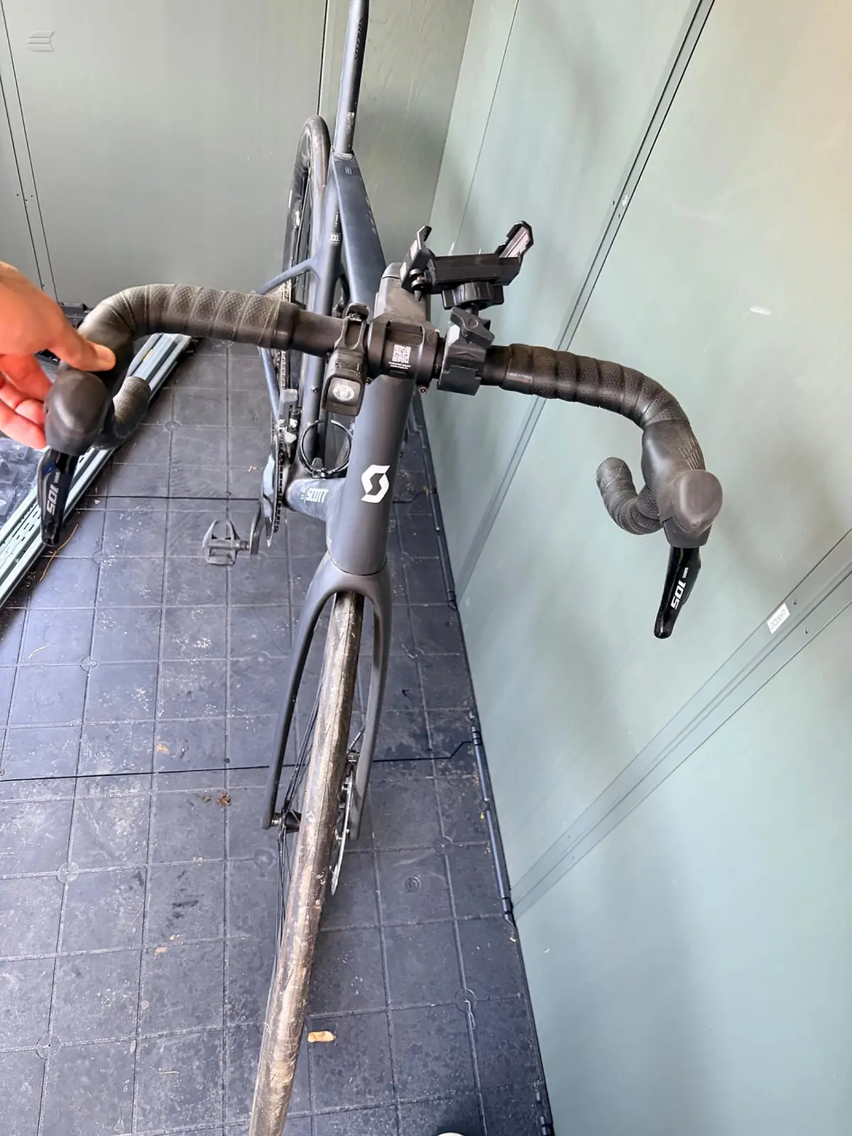 Scott gravel bike handlebars and drivetrain, top-down view on tiled floor, showing drop bars with bar tape, shifters, and front derailleur.
