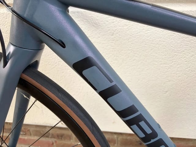 Close-up of blue and black bicycle frame tubing and down tube detail, non-drive side, against a light brick wall.