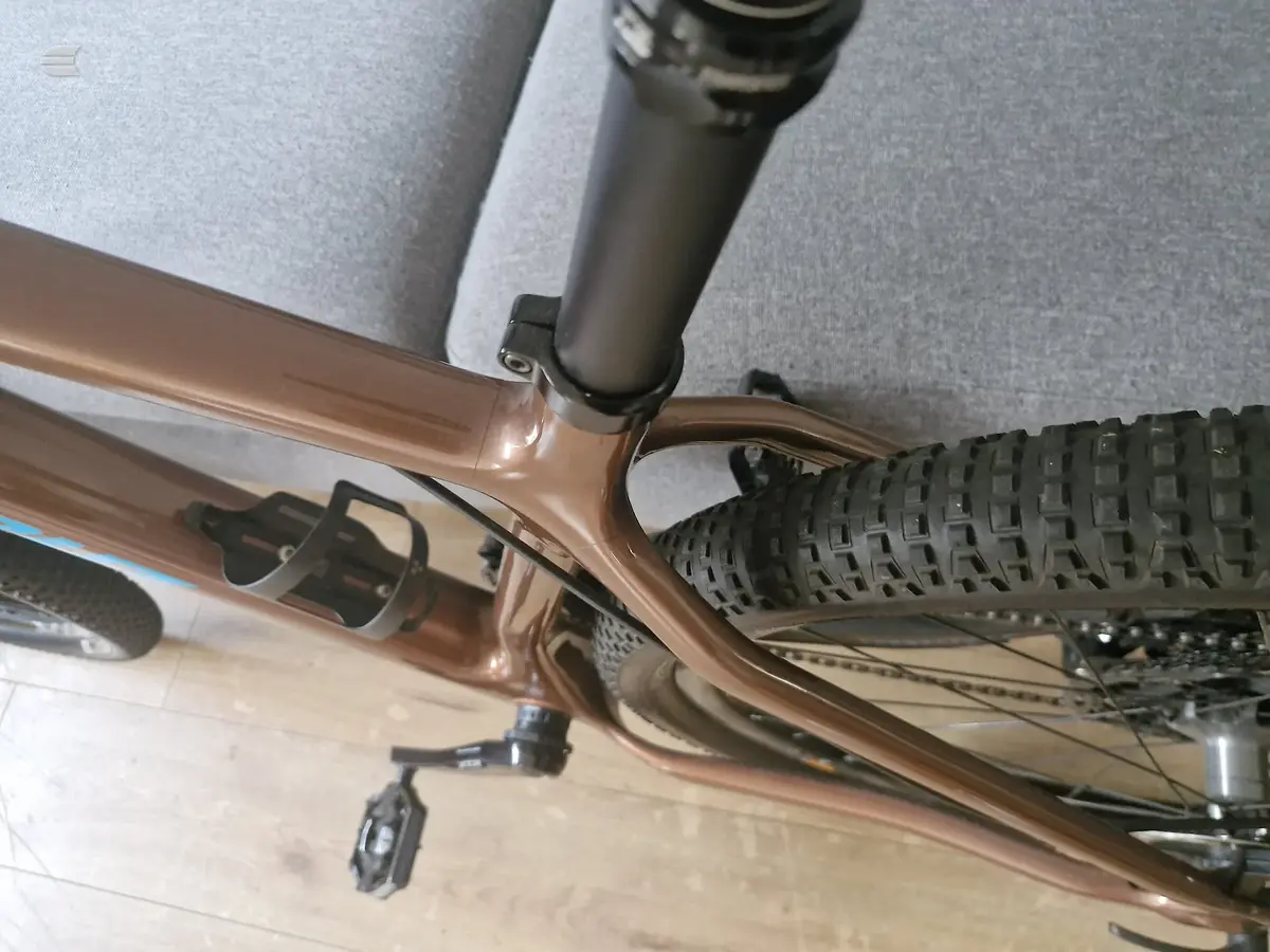 Brown gravel or hybrid bike on wooden floor, drive side, indoors against grey wall and furniture.