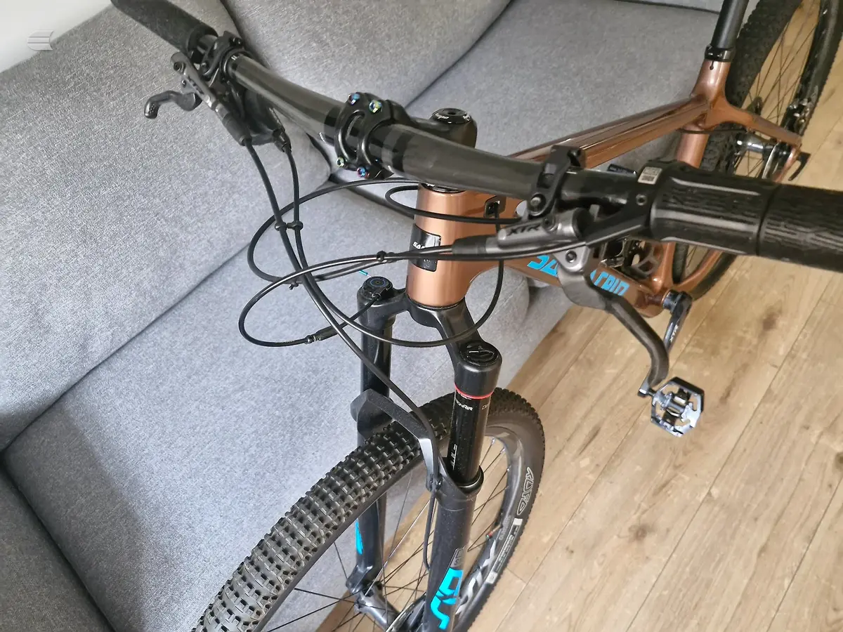 Blue and black hardtail mountain bike indoors on wooden floor, non-drive side view, leaning against grey sofa.