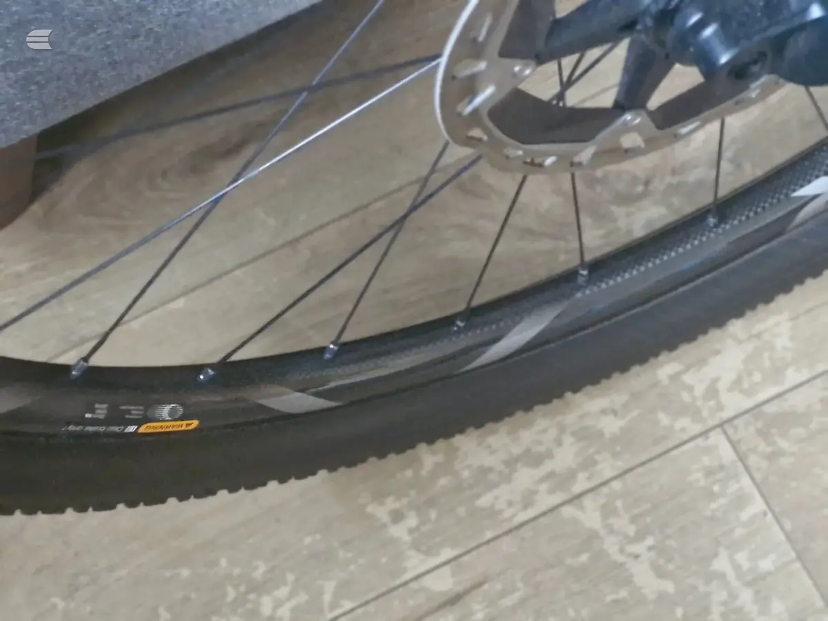 Close-up of a bicycle wheel with spokes and tyre on wooden flooring, non-drive side, indoors.
